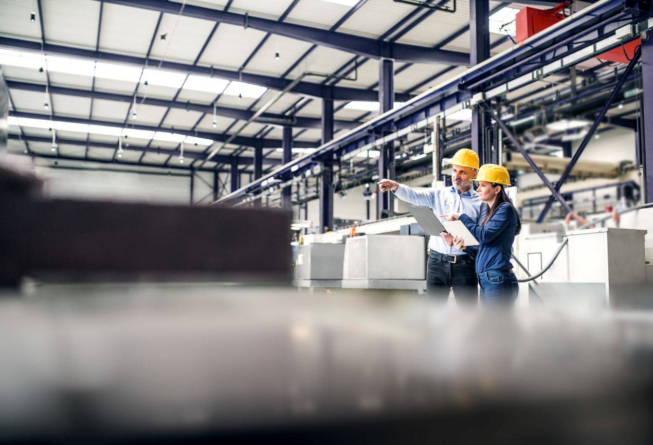 Zwei Ingenieure mit Helmen diskutieren in einer Lagerhalle über die Planung von Lagerlösungen, einschließlich wasserdichter Lagerzelte