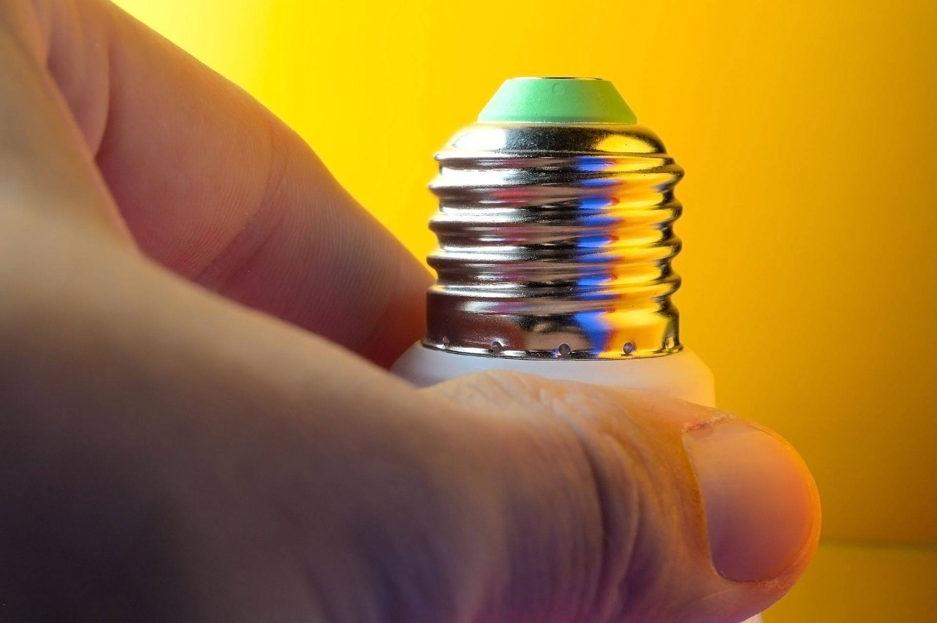 Hand haelt LED Leuchtmittel mit E14 Gewinde vor gelbem Hintergrund – Detailaufnahme der Schraubfassung